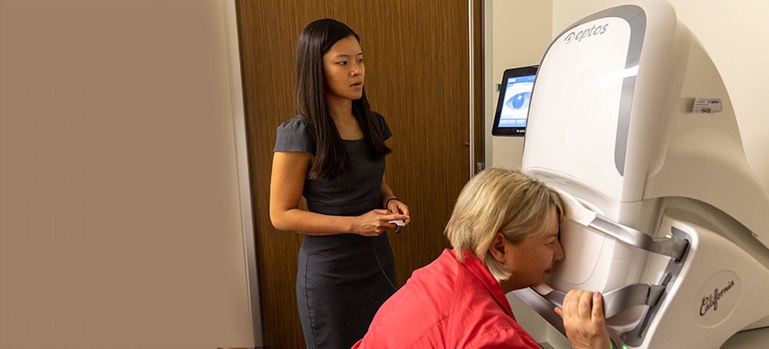Image shows woman having eye exam with optometrist watching on.